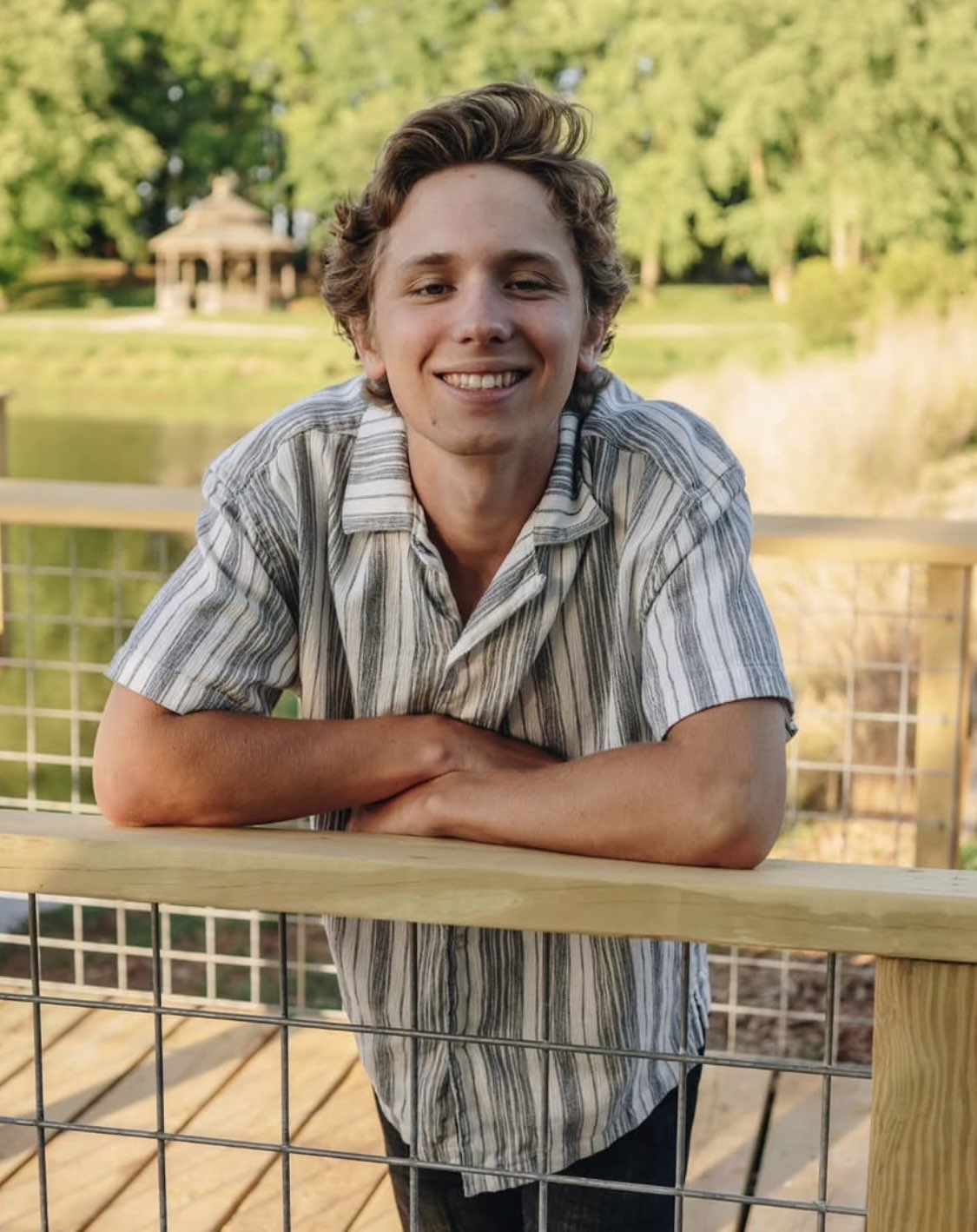 Ryder Mann smiling, leaning on a wooden railing by a pond